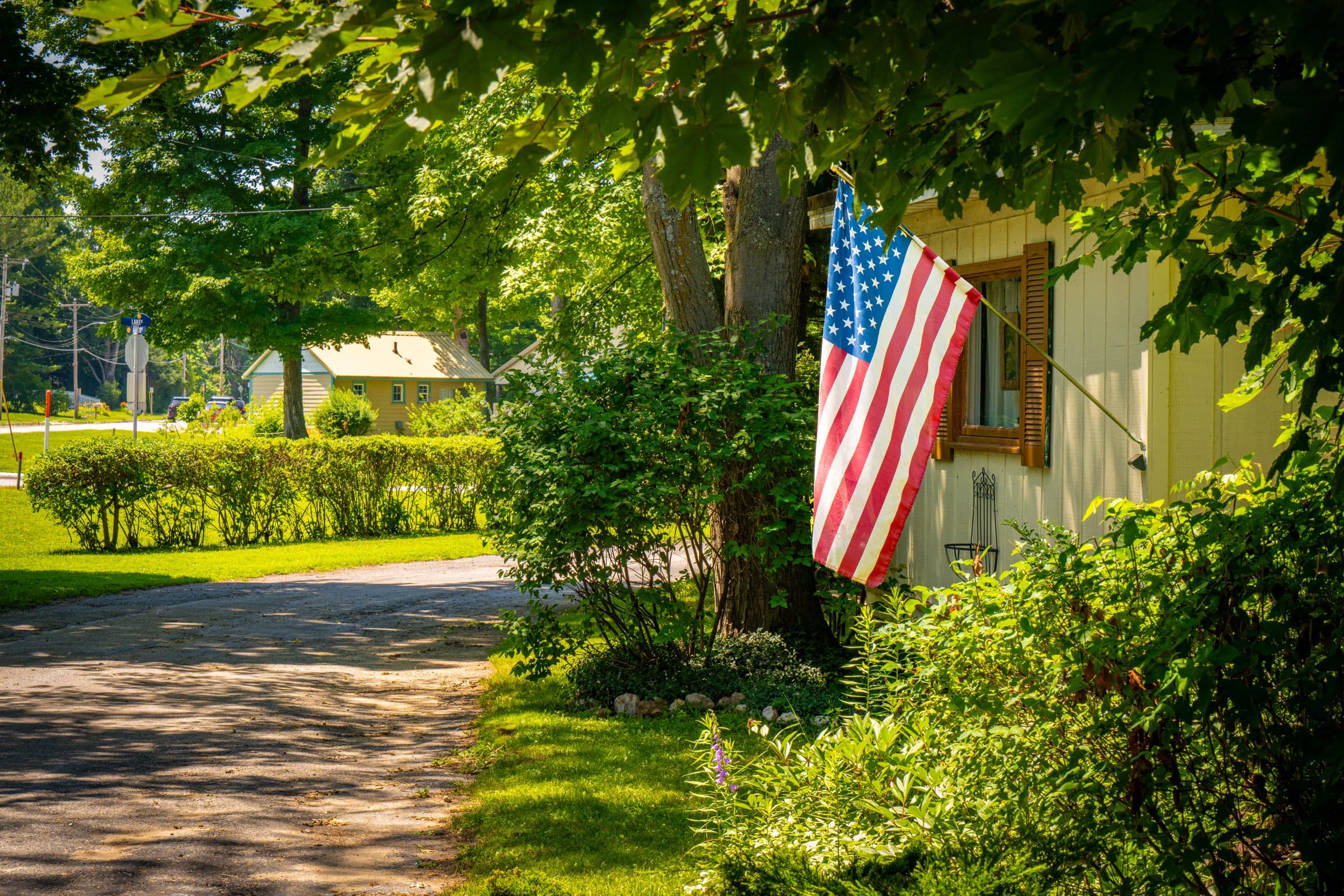An American flag hanging from a home beside a shaded lane through Vacation Village