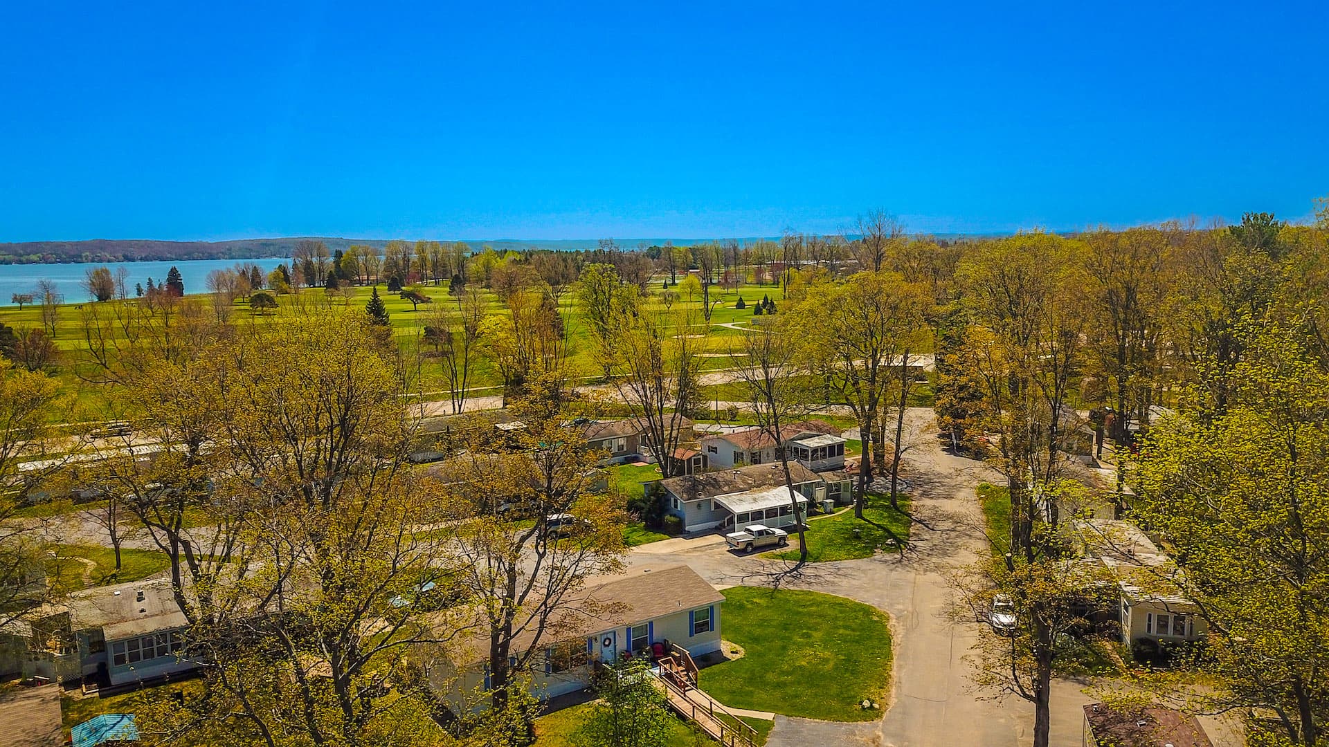 Aerial view over the homes and wooded streets of Vacation Village, with the golf course and Bass Lake beyond